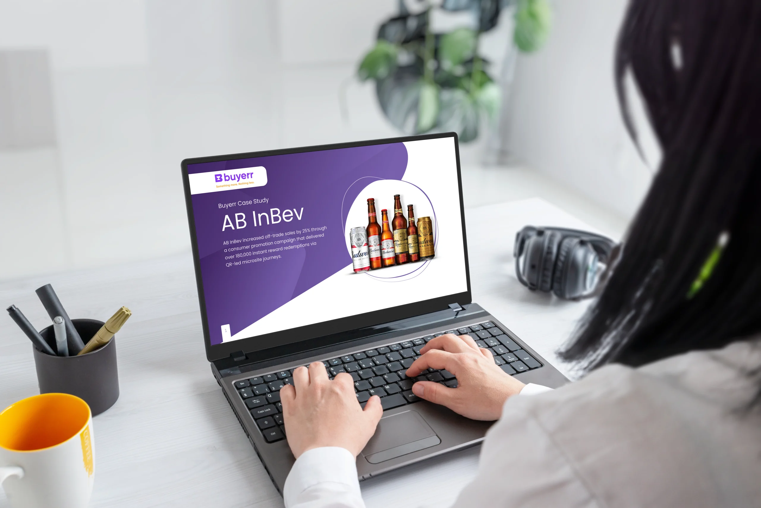 Over-the-shoulder view of a person using a laptop at a bright desk. The screen displays the Buyerr AB InBev case study slide with Budweiser product images.